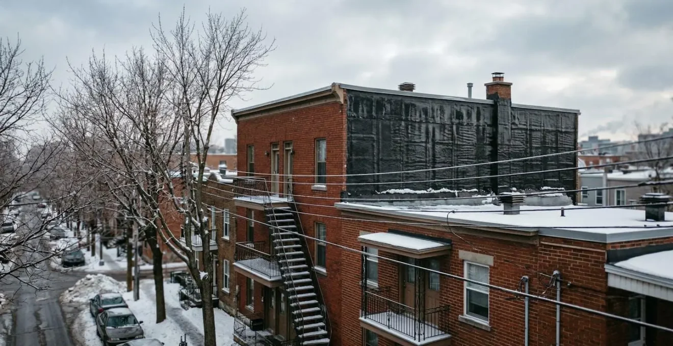 Vue en contre-plongée d'un toit plat de triplex montréalais sous un ciel d'hiver nuageux, texture de membrane visible sur la surface