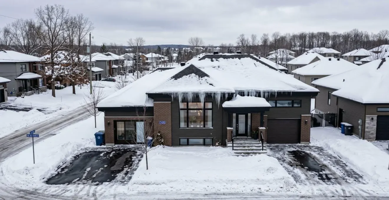 Toiture résidentielle québécoise recouverte de neige avec formation de glaçons sur les bordures par temps hivernal nuageux
